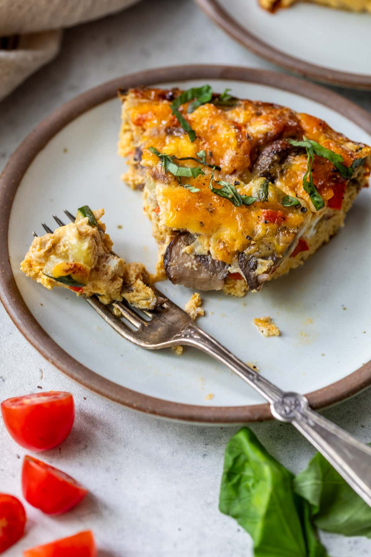 a fork taking a bite of a slice of crustless vegetable quiche on a white plate.