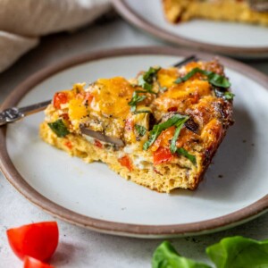 a slice of a crustless vegetable quiche on a white plate.
