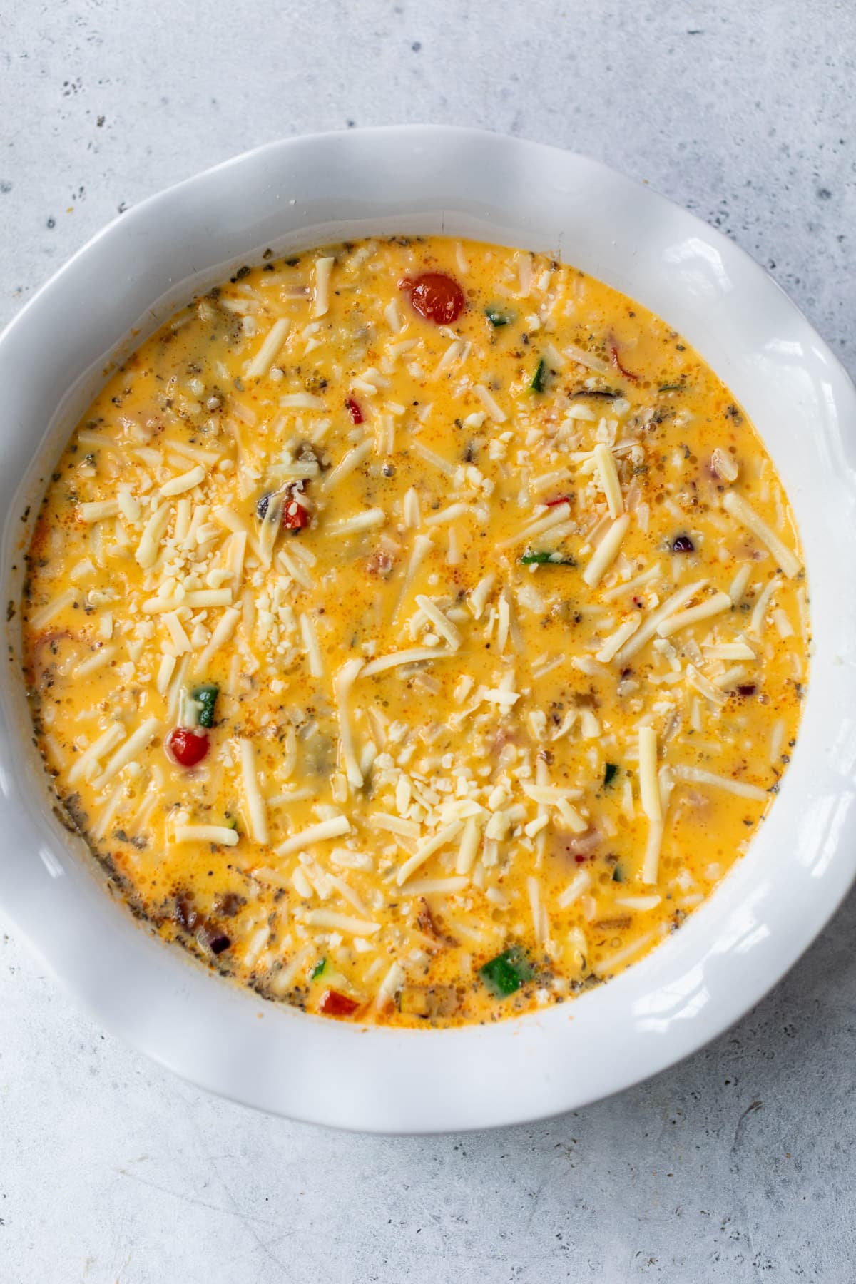 the liquid egg filling for a vegetable quiche in a large white pie plate.