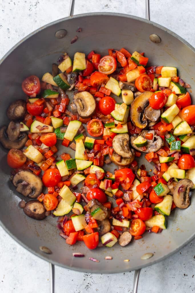 cooking the vegetables for a vegetable quiche in a large skillet.
