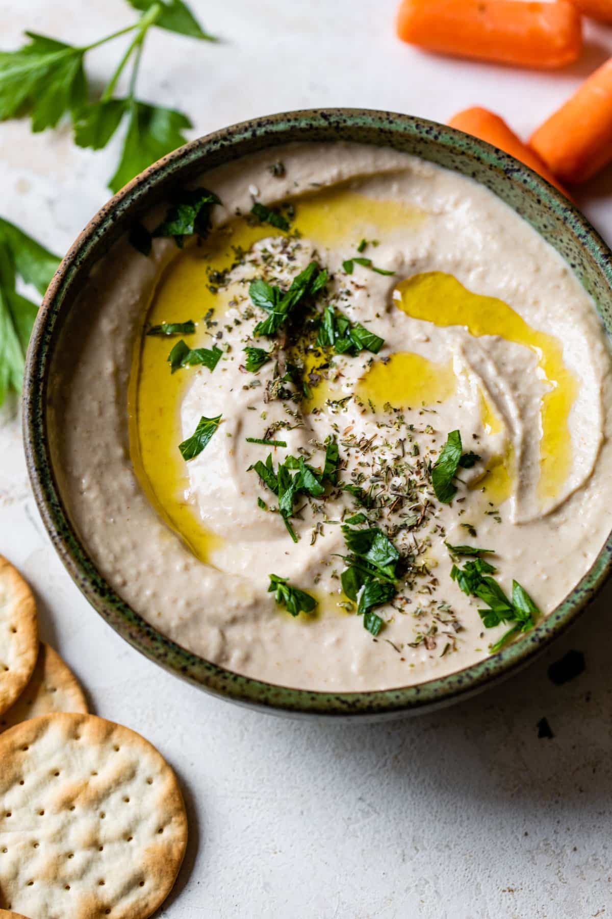 white bean hummus in a bowl with a cracker and olive oil drizzled on top