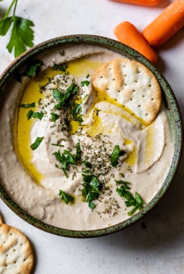 white bean hummus in a bowl with a cracker and olive oil drizzled on top