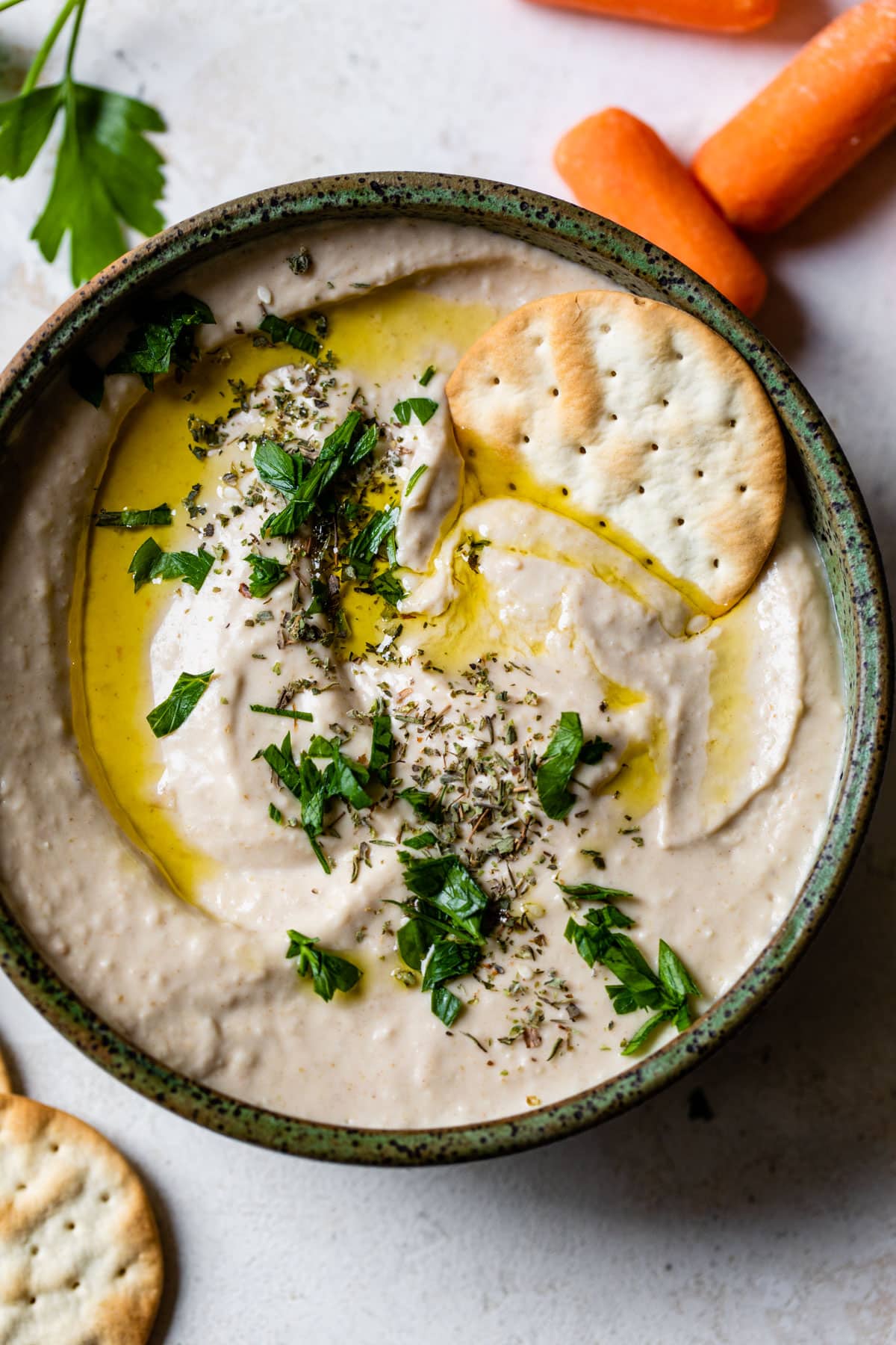 white bean hummus in a bowl with a cracker and olive oil drizzled on top